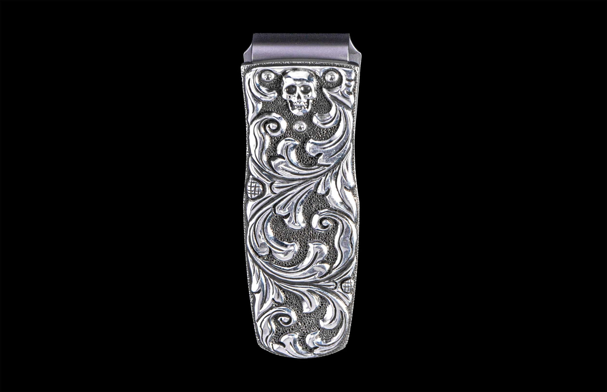 Silver money clip with an etched skull design and ornate scrolling on a textured background.