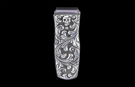 Silver money clip with an etched skull design and ornate scrolling on a textured background.