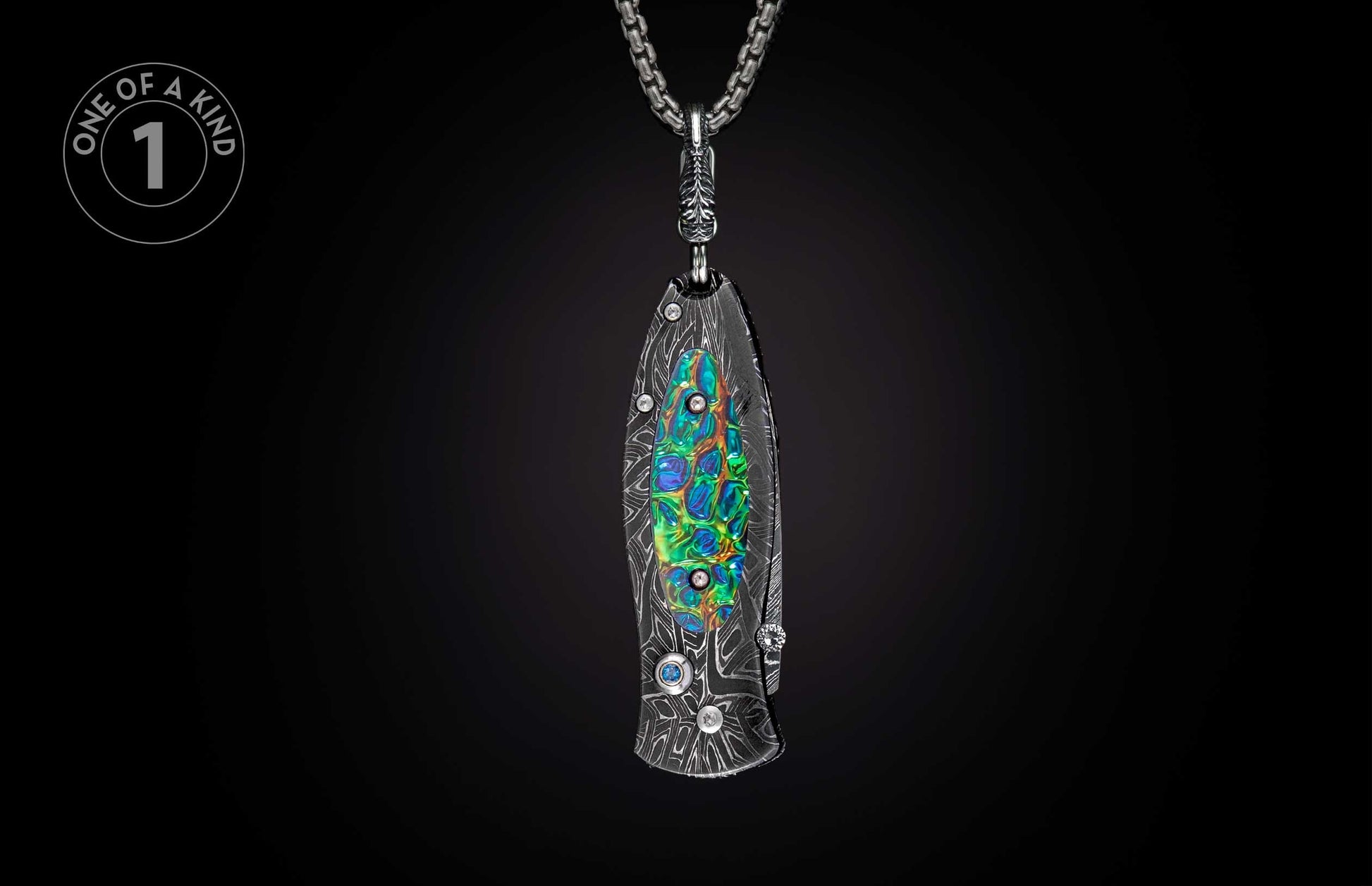 Folding knife with dark patterned handle, vibrant iridescent inlay, and gemstone accents, suspended from a silver chain.