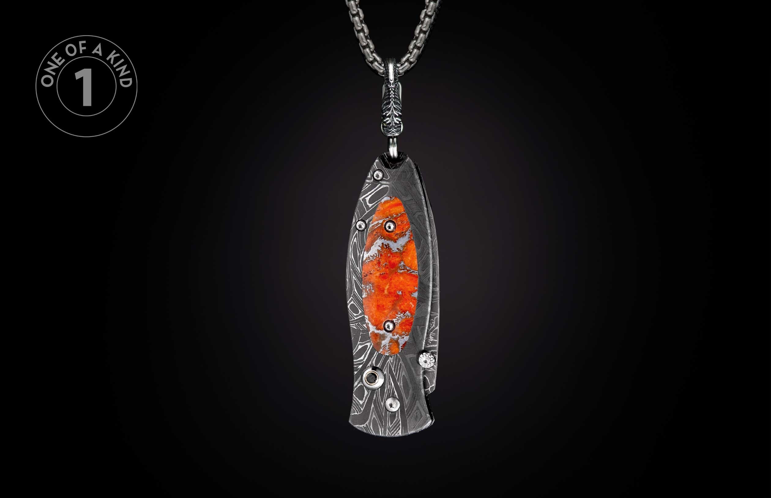 Decorative knife with dark Damascus pattern, orange stone inlay, and small gemstone, hanging from a silver chain.