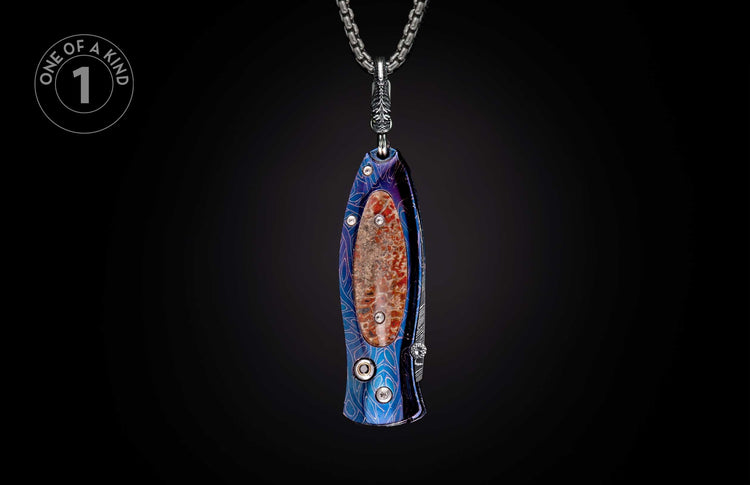 Ornate knife with a blue and purple patterned handle, red fossil inlay, and three clear stones, hanging from a silver chain.