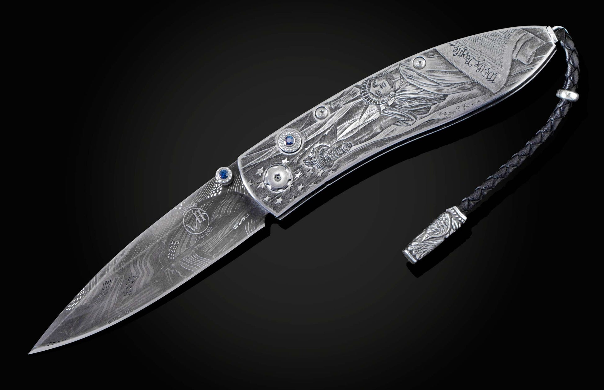 Handcrafted pocket knife from William Henry featuring a stainless steel frame hand-engraved with images of the Statue of Liberty and set with blue sapphires. The blade is hand-forged damascus steel.