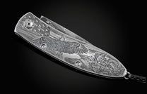 Handcrafted pocket knife from William Henry featuring a stainless steel frame hand-engraved with images of an eagle and soldiers and set with blue sapphires. The blade is hand-forged damascus steel.
