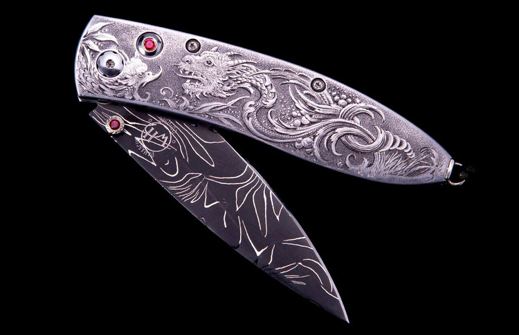 Silver engraved pocket knife with a detailed dragon, red gemstone accents, and a dark patterned blade.
