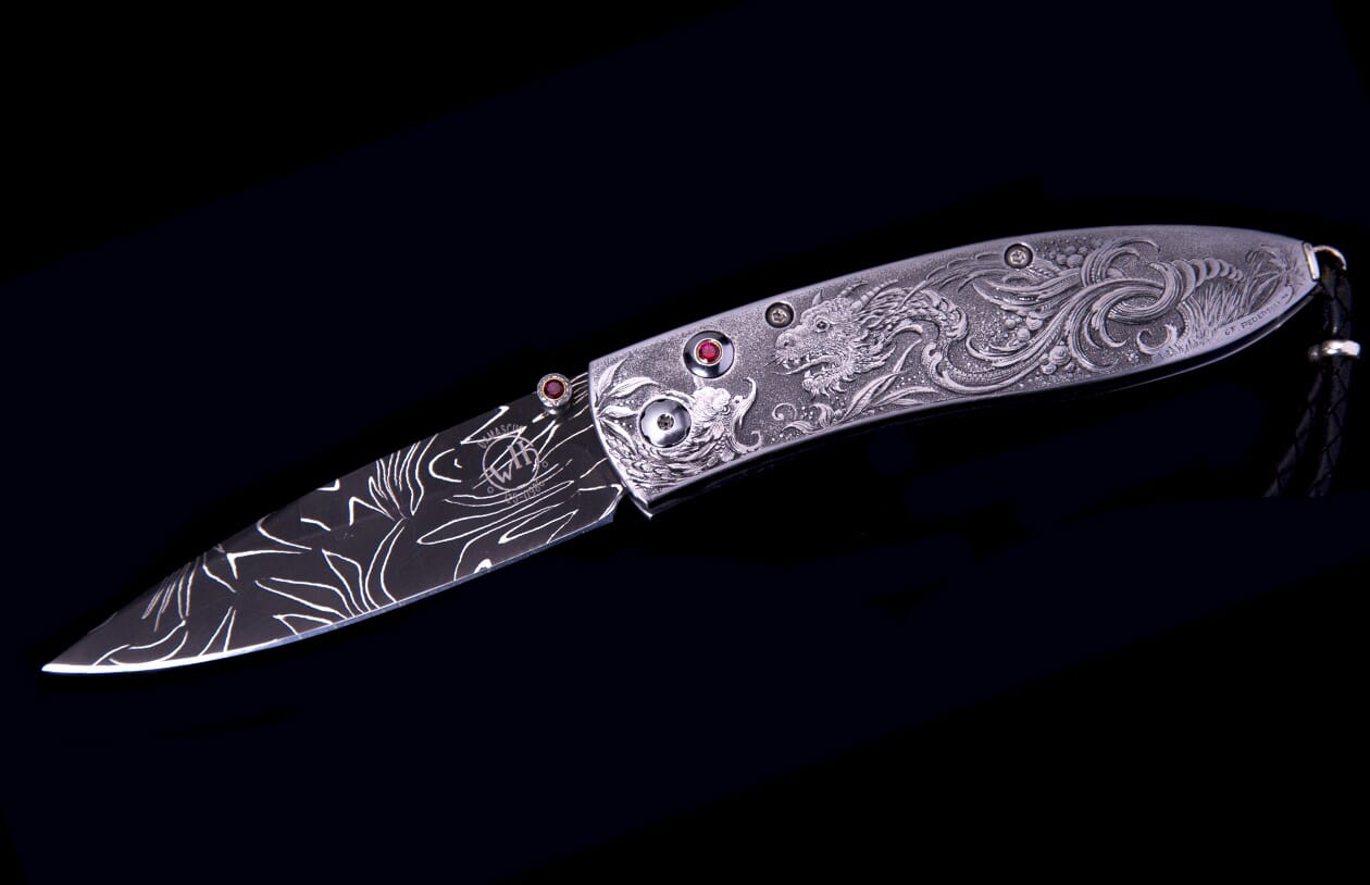 Ornate silver-toned folding knife with Damascus patterned blade and intricate dragon engraving on the handle, accented by red gemstones.