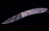 Ornate silver-toned folding knife with Damascus patterned blade and intricate dragon engraving on the handle, accented by red gemstones.