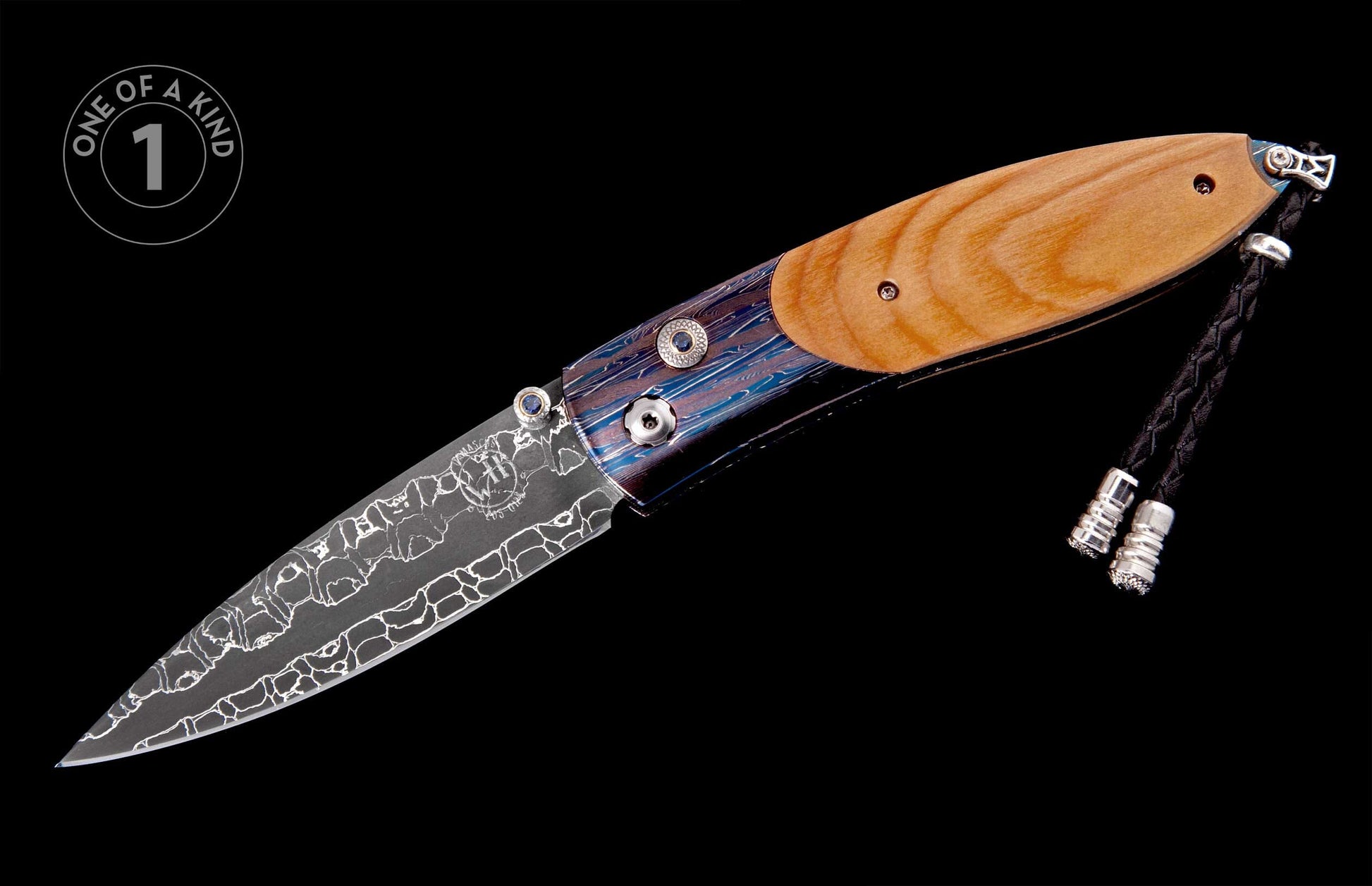 Folding knife with a light brown wooden handle and blue and purple patterned metal, a patterned blade, and a black braided leather lanyard with silver tips.