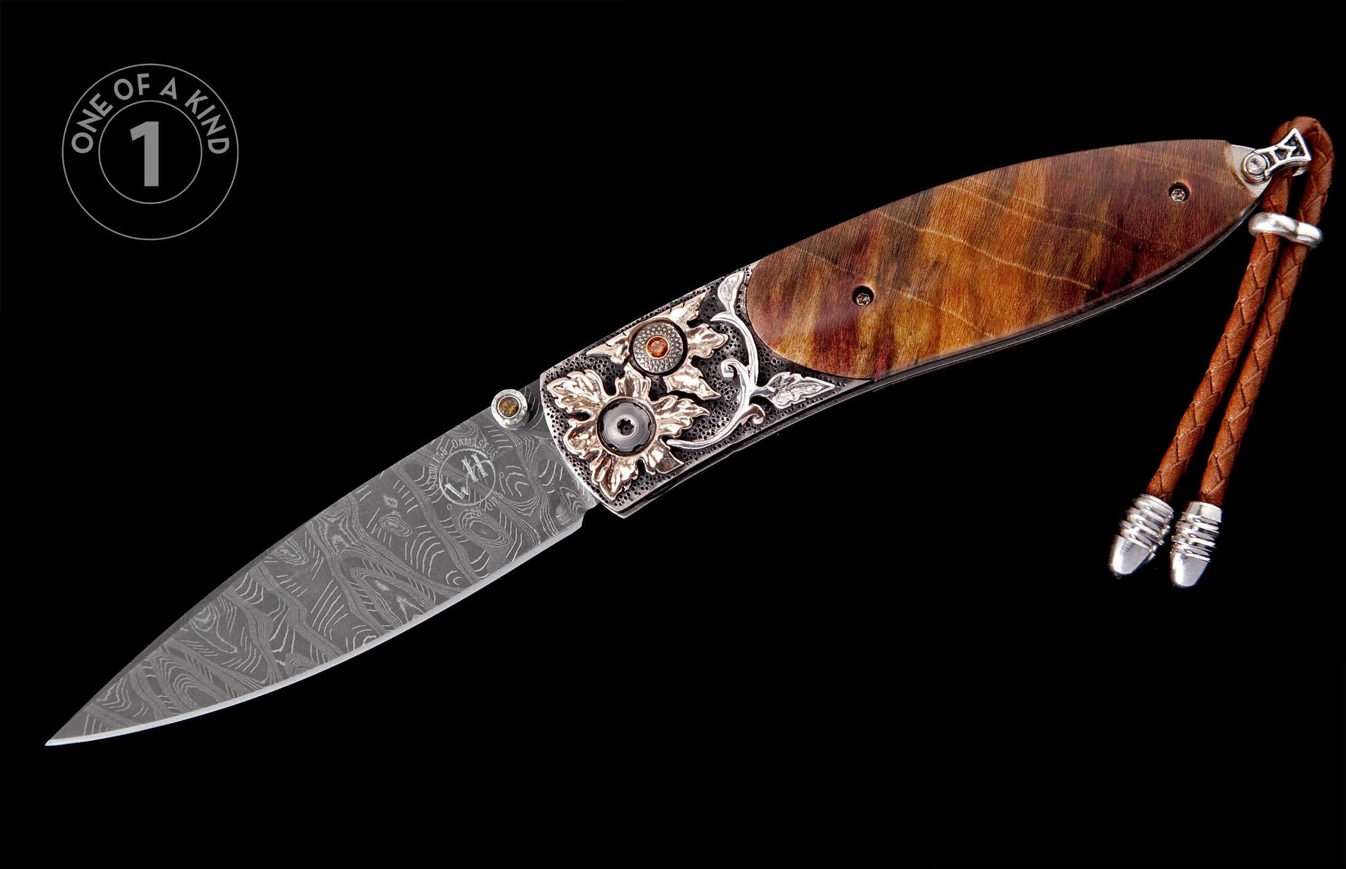 Folding knife with a Damascus steel blade, engraved silver bolster with orange gems, brown wood handle, and a braided leather lanyard.