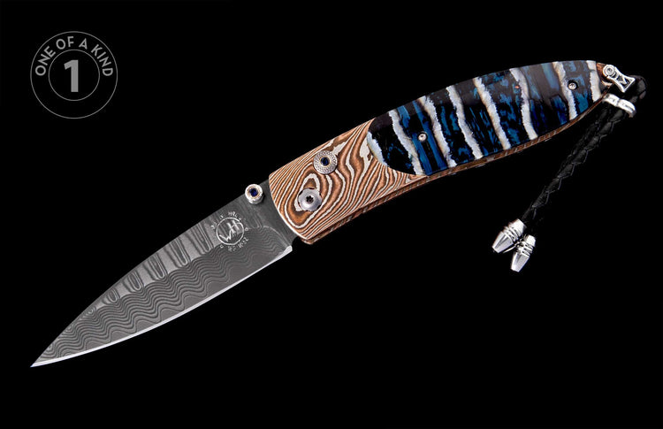 Damascus steel knife with wavy wooden grain and blue-striped iridescent handle, accented by blue gem fasteners and a black leather lanyard.