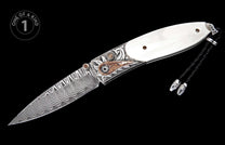 Ornate folding knife with a wavy Damascus steel blade, white handle, and detailed silver and copper engraved bolster, featuring a black braided lanyard.