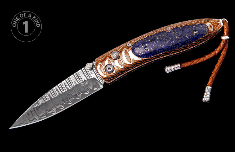 A folding knife with a Damascus blade and ornate handle featuring a blue lapis lazuli inlay, detailed hardware, and a braided brown leather lanyard.
