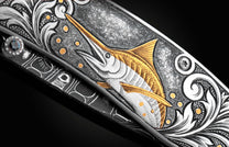 Handcrafted pocket knife from William Henry features a hand-engraved image of a Marlin with 24K gold inlays and set with dark Kashmir blue topaz and a hand forged Damascus steel blade.