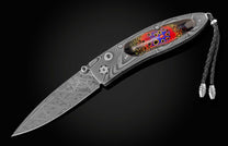  inlaid with enamel artistry by Little Lake Metals. The blade is hand-forged Damascus and the button lock and thumb stud are set with spinel gemstones.