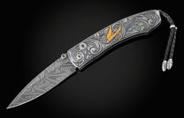 Hand forged Damascus steel blade pocket knife from William Henry. The knife is hand-engraved handle with 24K gold inlays depicting a floral design and a fly fishing lure. The knife is displayed fully open on a black background.