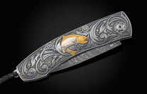 Hand forged Damascus steel blade pocket knife from William Henry. The knife is hand-engraved handle with 24K gold inlays depicting a floral design and a fly fishing lure. The knife is displayed closed on a black background.
