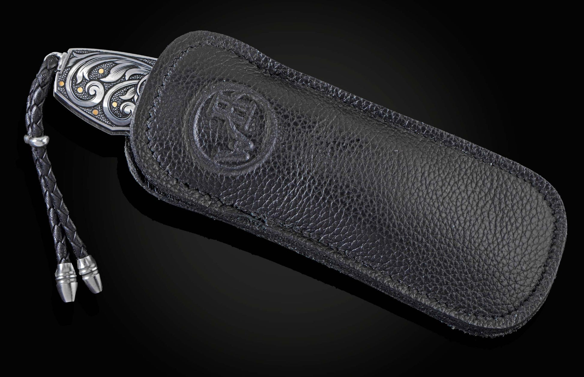 Hand forged Damascus steel blade pocket knife from William Henry. The knife is hand-engraved handle with 24K gold inlays depicting a floral design and a fly fishing lure. The knife is displayed in a leather case  on a black background.
