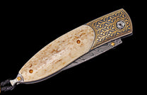 Custom folding knife featuring a light bone handle, gold engraved dark metal, and patterned Damascus steel blade.