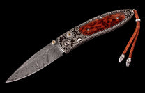 Ornate custom folding knife with a Damascus steel blade, decorative silver handle, reddish-brown wood inlay, and braided leather lanyard.