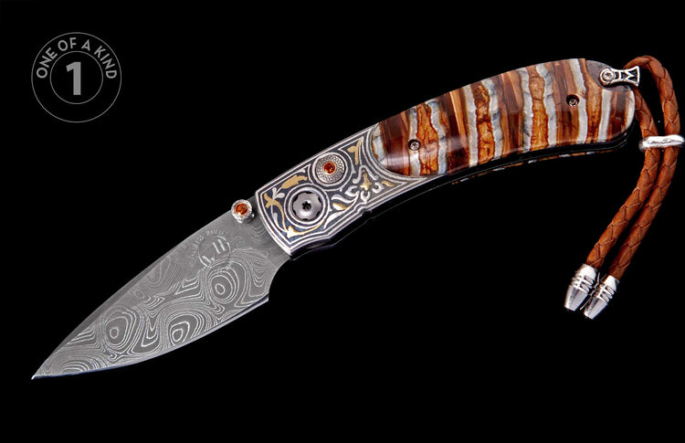 Damascus steel folding knife with swirling patterns, ornate silver and gold engraved handle featuring orange gems, striped brown and white handle scales, and a brown leather lanyard.