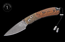 Folding knife with Damascus blade, engraved bronze bolster accented by amber gems, tiger stripe wood handle, and black lanyard with silver tips.