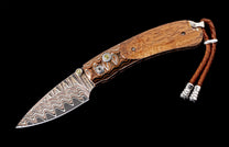 Folding knife with a patterned Damascus blade and wooden handle by B09 Pono, featuring decorative pins with yellow gems and a brown braided leather lanyard.