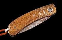 A folding knife with a brown wooden handle and Damascus steel accents by B09 Pono, showing wavy silver and copper patterns and a braided leather lanyard.