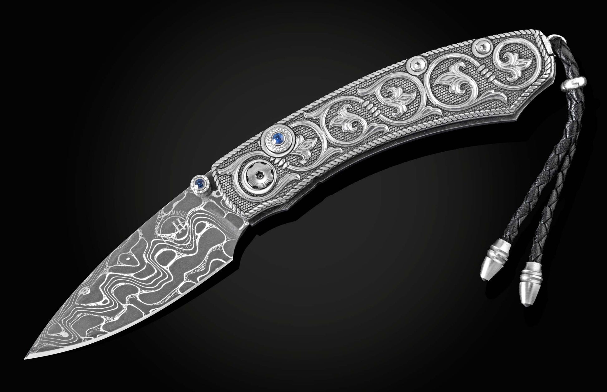 Handcrafted pocket knife from William Henry features hand and laser engraved handles set with sapphire gemstones and a blade of hand-forged Damascus steel.