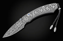 Handcrafted pocket knife from William Henry features hand and laser engraved handles set with sapphire gemstones and a blade of hand-forged Damascus steel.