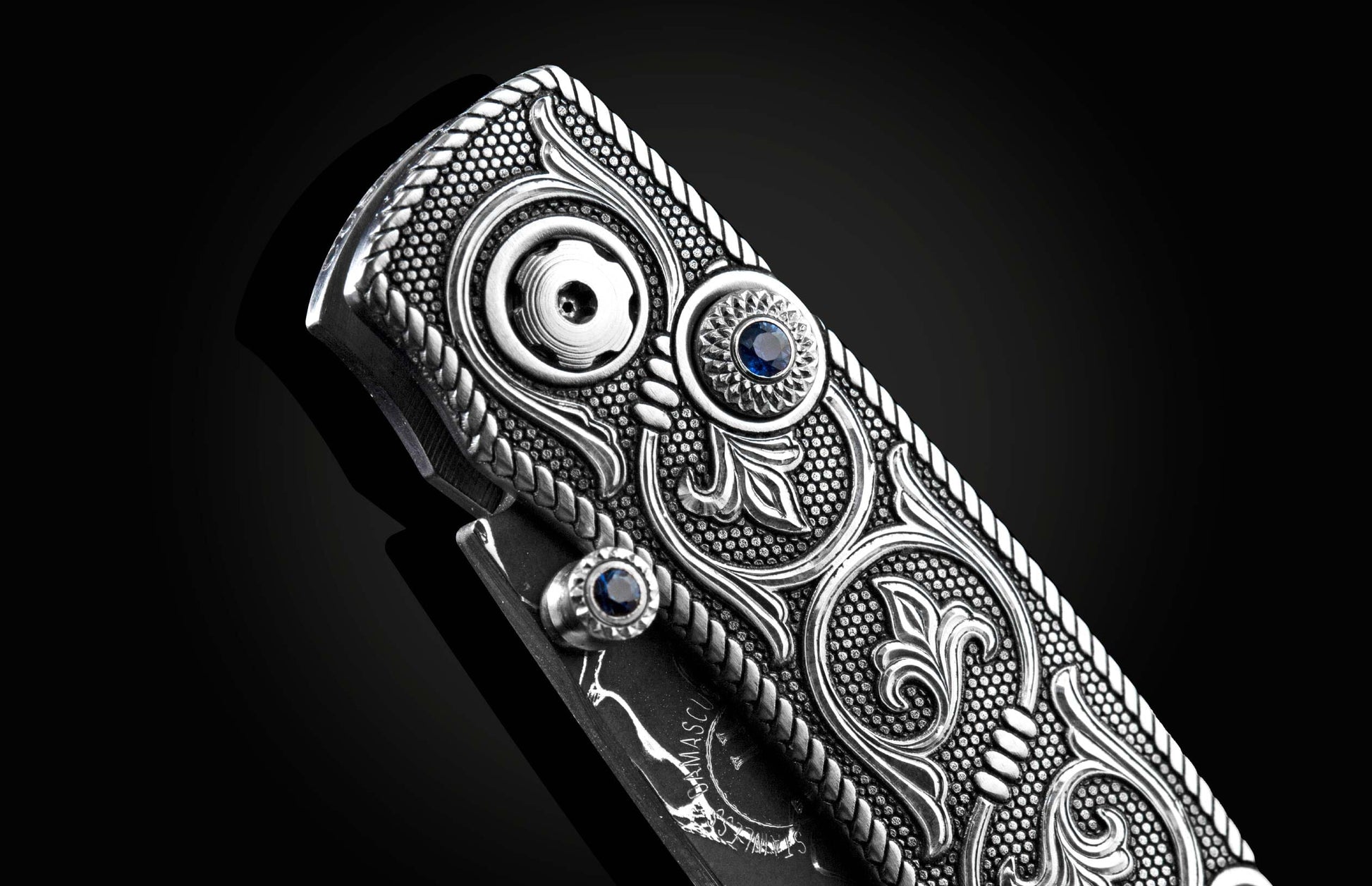 Handcrafted pocket knife from William Henry features hand and laser engraved handles set with sapphire gemstones and a blade of hand-forged Damascus steel.