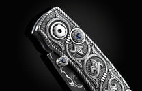 Handcrafted pocket knife from William Henry features hand and laser engraved handles set with sapphire gemstones and a blade of hand-forged Damascus steel.