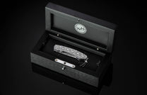 Handcrafted pocket knife from William Henry features hand and laser engraved handles set with sapphire gemstones and a blade of hand-forged Damascus steel.