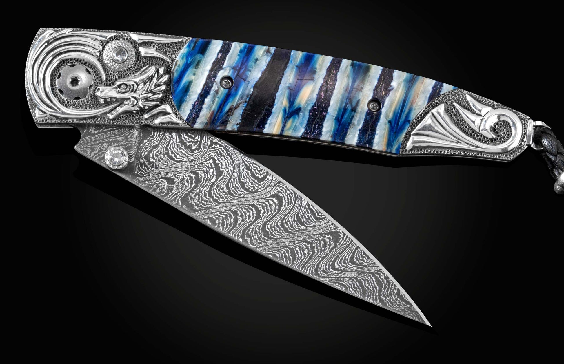 Handcrafted pocket knife from William Henry features a hand-carved sterling silver depicting a dragons head and tail, inlaid with blue Woolly Mammoth tooth, set with white topaz gemstones, and a hand forged Damascus steel blade.