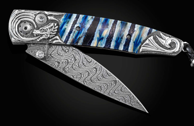 Handcrafted pocket knife from William Henry features a hand-carved sterling silver depicting a dragons head and tail, inlaid with blue Woolly Mammoth tooth, set with white topaz gemstones, and a hand forged Damascus steel blade.