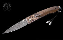 Damascus steel folding knife with a swirling blade pattern, ornate bronze bolster, and brown wood handle, featuring a black braided lanyard with silver beads.