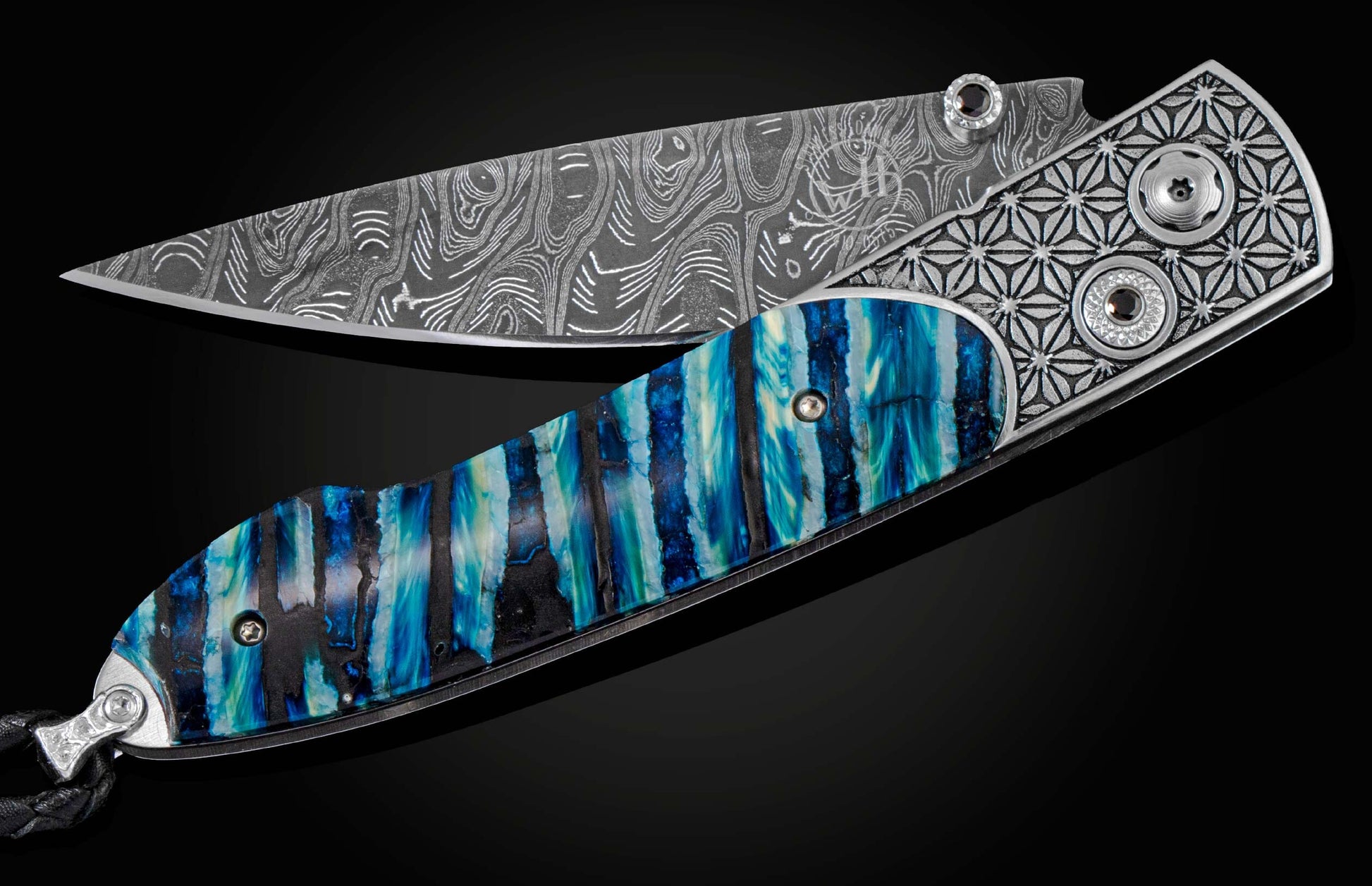 Handcrafted pocket knife from William Henry featuring a laser engraved stainless frame and scales of blue fossil Woolly Mammoth tooth. The blade is hand-forged damascus steel and the button lock and the thumb stud are set with spinel gemstones.