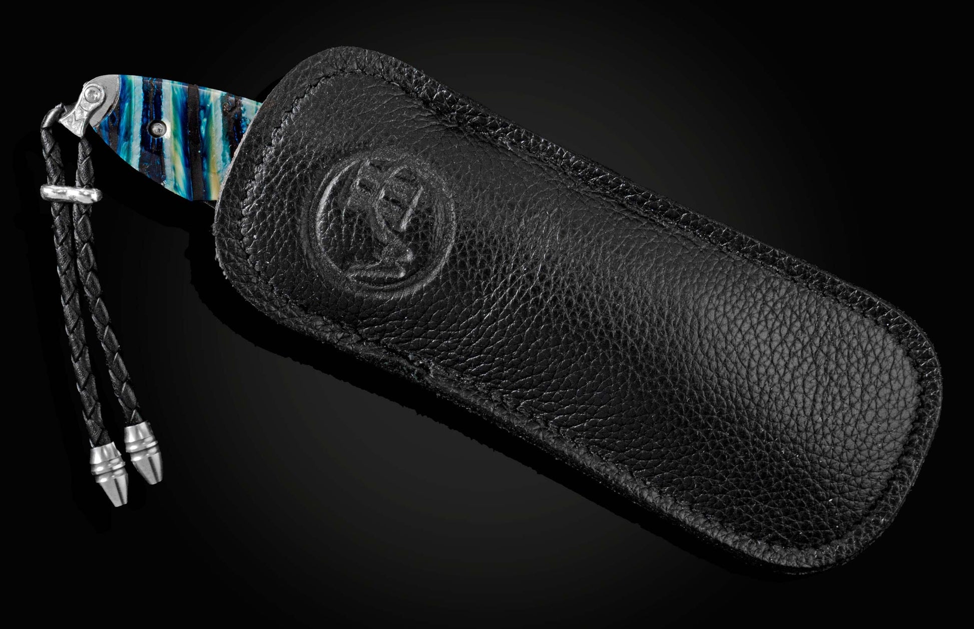 Handcrafted pocket knife from William Henry featuring a laser engraved stainless frame and scales of blue fossil Woolly Mammoth tooth. The blade is hand-forged damascus steel and the button lock and the thumb stud are set with spinel gemstones.