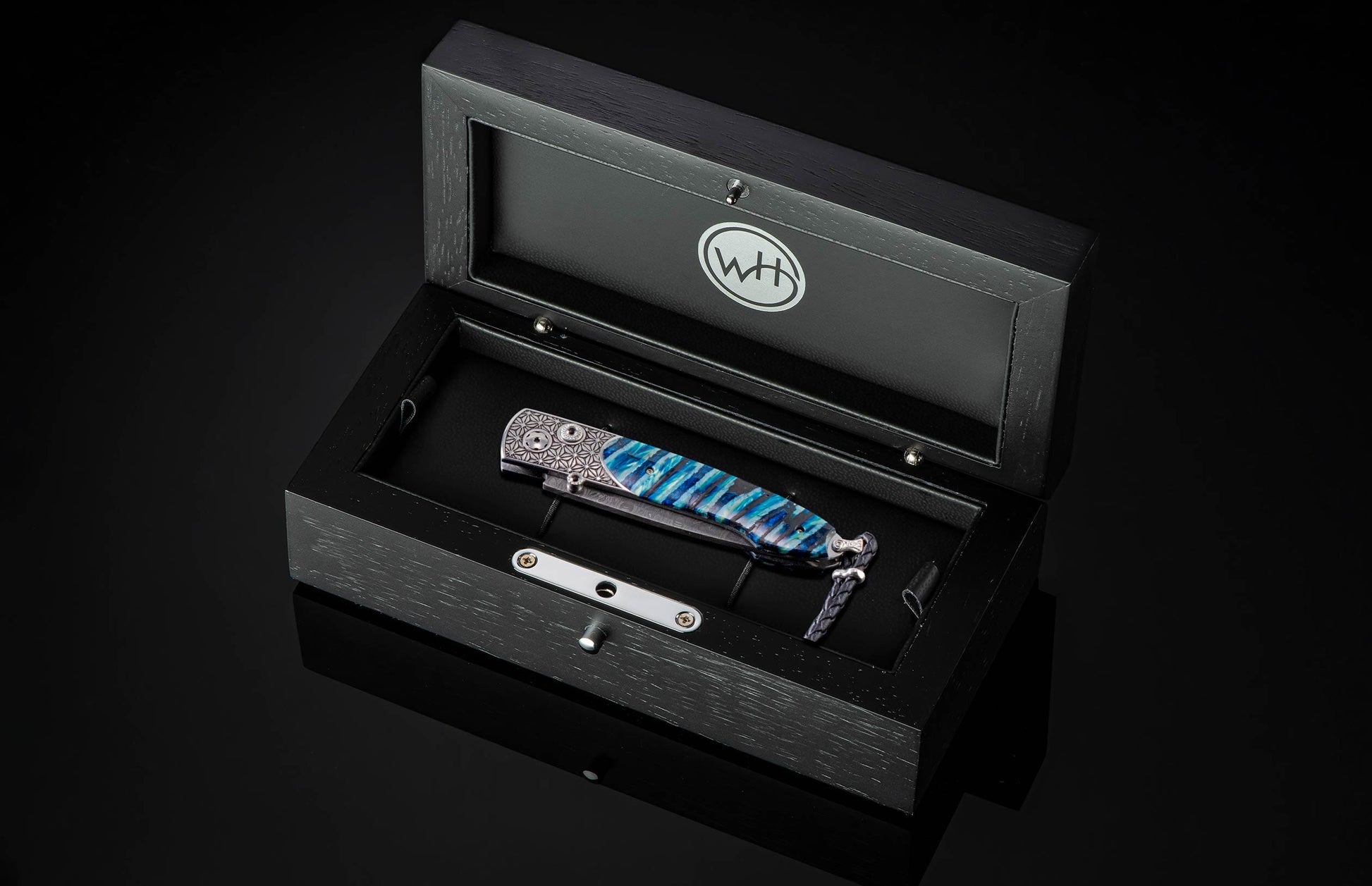 Handcrafted pocket knife from William Henry featuring a laser engraved stainless frame and scales of blue fossil Woolly Mammoth tooth. The blade is hand-forged damascus steel and the button lock and the thumb stud are set with spinel gemstones.