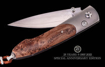 Silver blade folding knife with brown burl wood handle, metal accents, a blade logo, braided leather lanyard, and 25-year anniversary text.