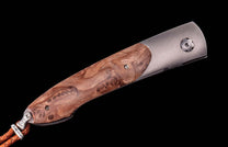 Closed pocket knife with a rich brown burl wood handle, brushed metal bolster, and a braided leather lanyard.