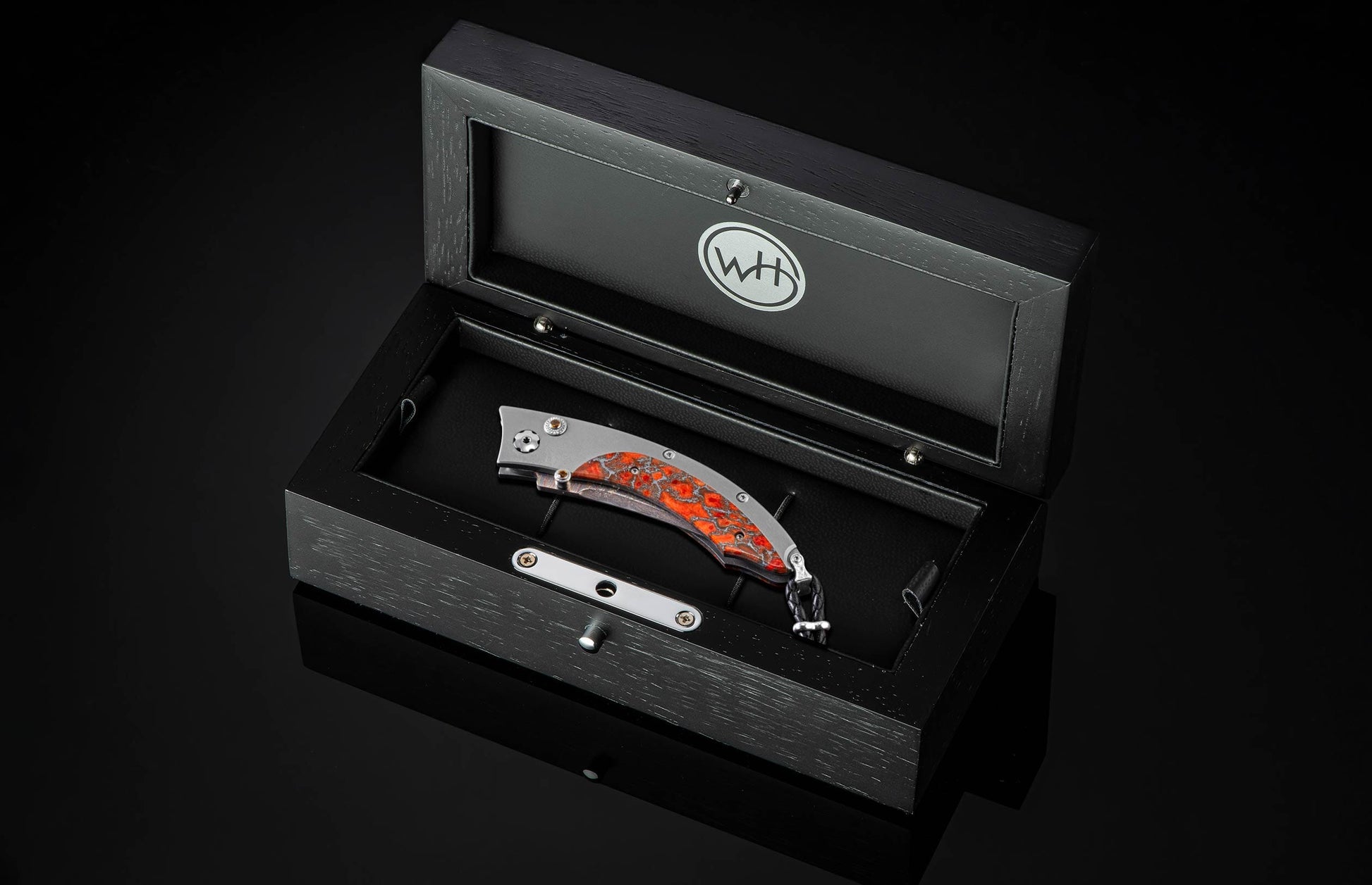 Handcrafted pocket knife from William Henry features a titanium frame inlaid with orange and red zinc matrix Apple Coral. The button lock and the thumb stud have been set with citrine gemstones and the hand forged Damascus steel blade has a copper wave pa