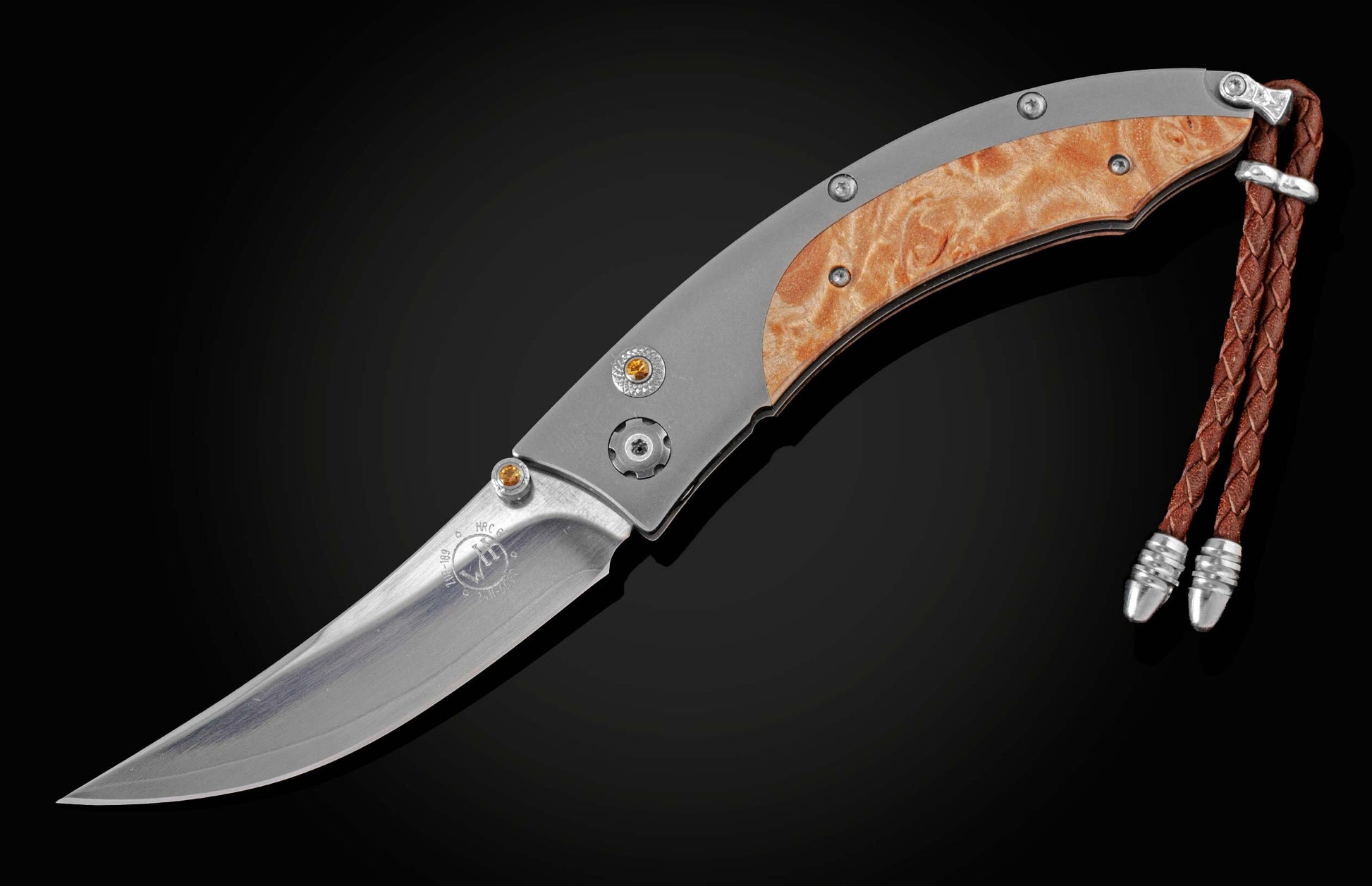 Handcrafted pocketknife from William Henry features a titanium frame inlaid with maple burl wood. The button lock and the thumb stud have been set with fine citrine gemstones. The knife is shown fully open on a black background.
