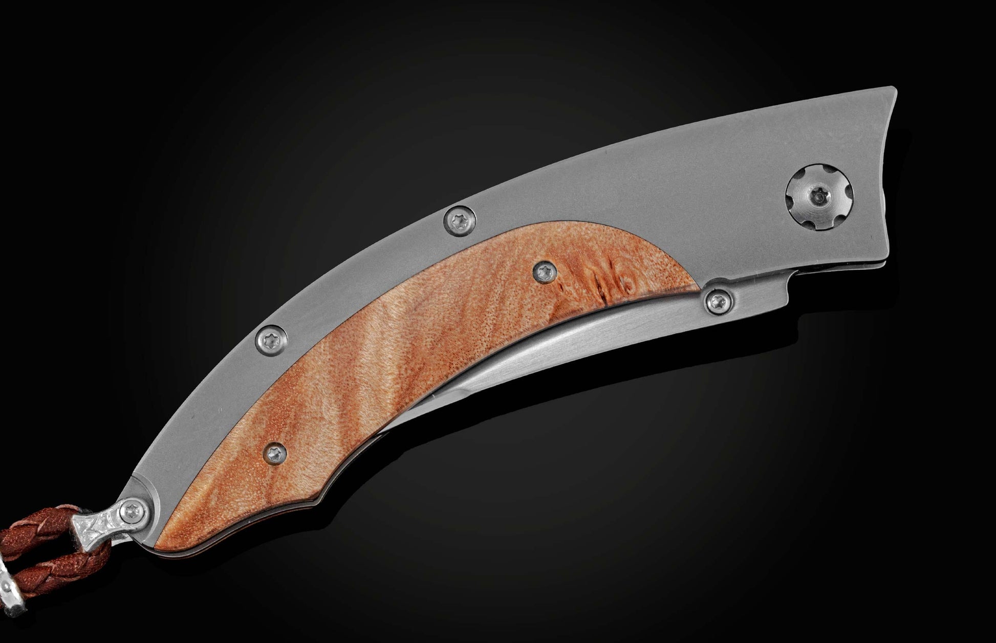 Handcrafted pocketknife from William Henry features a titanium frame inlaid with maple burl wood. The button lock and the thumb stud have been set with fine citrine gemstones. The knife is shown closed on a black background.