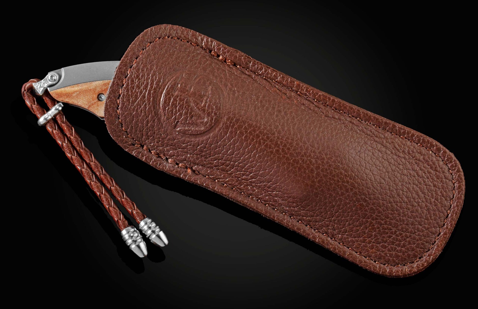 Handcrafted pocketknife from William Henry features a titanium frame inlaid with maple burl wood. The button lock and the thumb stud have been set with fine citrine gemstones. The knife is shown in a custom leather case on a black background.