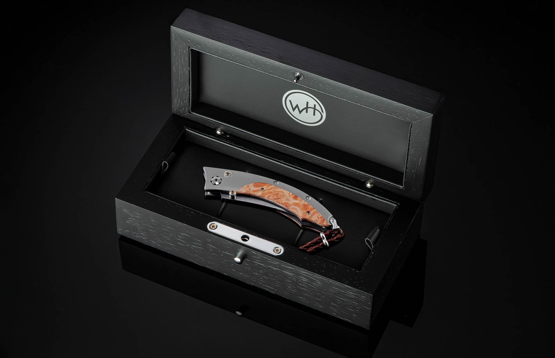 Handcrafted pocketknife from William Henry features a titanium frame inlaid with maple burl wood. The button lock and the thumb stud have been set with fine citrine gemstones. The knife is shown in a custom display case on a black background.