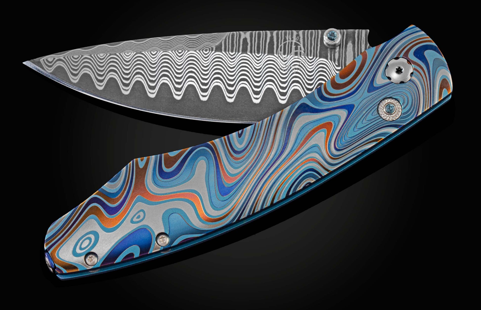 Unique pocket knife from William Henry in swirling colors on laser-engraved titanium with hand-forged damascus blade and blue topaz gemstones. The knife is displayed partially open on a black background.