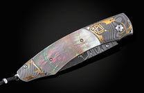 Handcrafted knife from William Henry features Hand-forged Damascus steel bolsters with gold inlays. The scales are black lip pearl