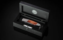  inlaid with reclaimed wood from the seats of Ohio Stadium. The blade is hand-forged Damascus steel and the button lock and the thumb stud are set with rubies. The knife is shown open