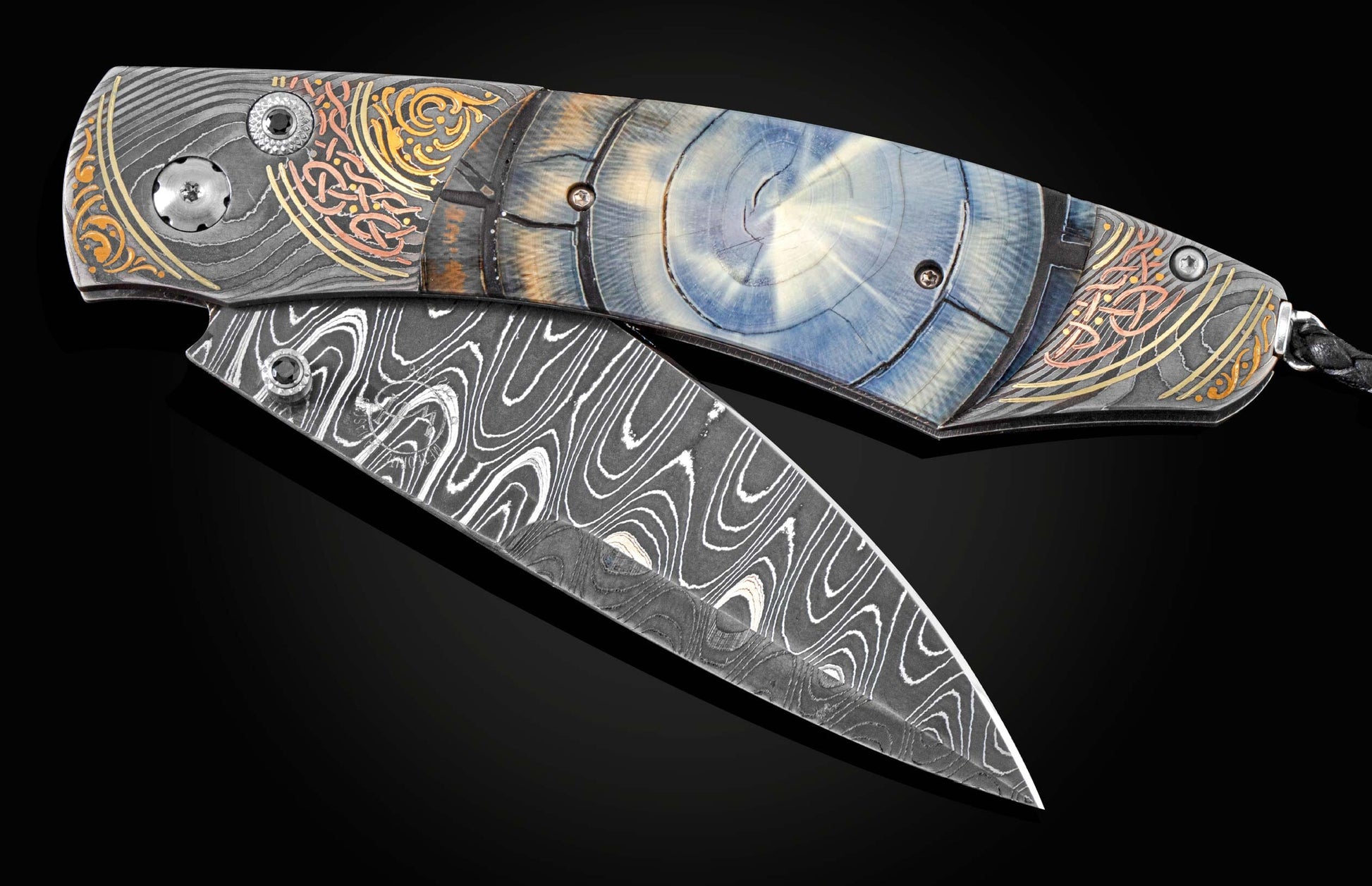 Handcrafted pocket knife from William Henry features a hand-forged damascus steel frame with 24K and 22K yellow gold, 18K green gold, and copper with spinel gemstones., inlaid with fossil Woolly Mammoth tusk. The blade is hand forged damascus steel which 