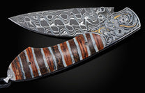 Folding knife with a patterned Damascus blade, engraved bolster with gold and black gemstones, and a striped brown and white handle.