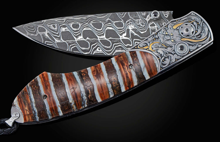 Folding knife with a patterned Damascus blade, engraved bolster with gold and black gemstones, and a striped brown and white handle.